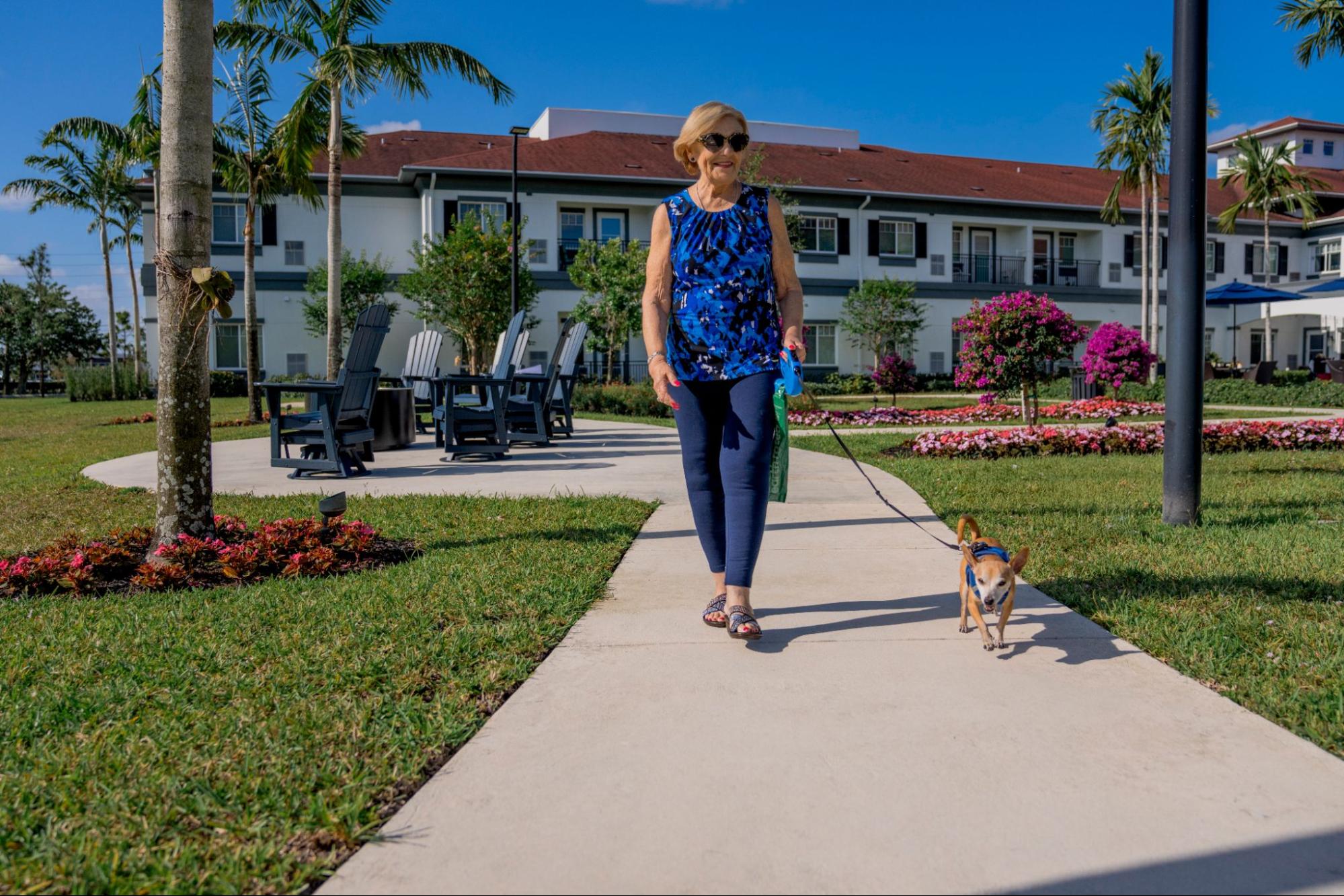 Female resident walks small dog through paths at Alamar Senior Living